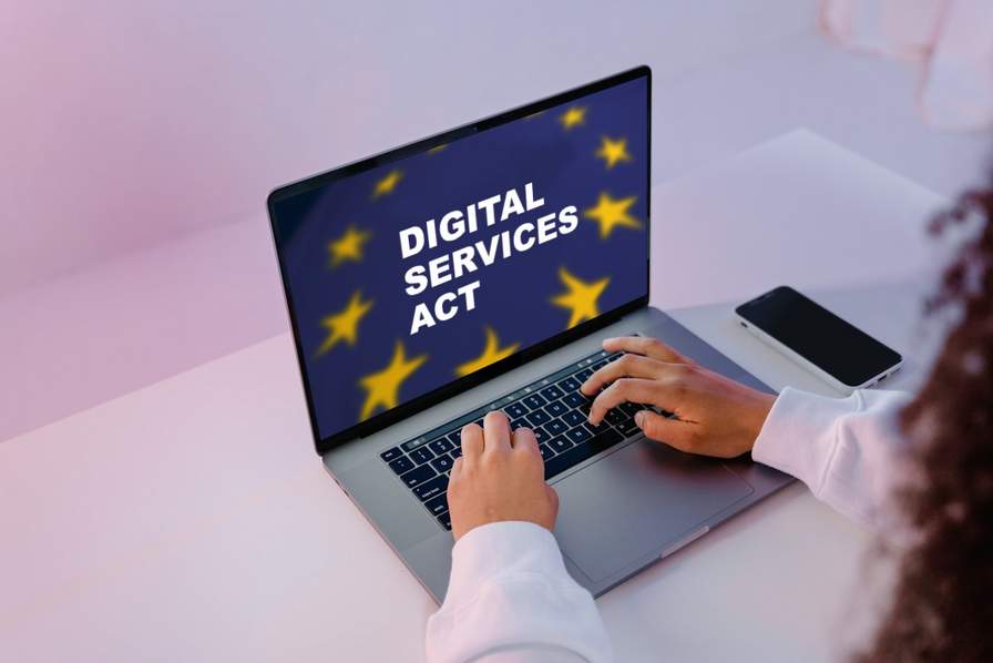 EU's Digital Services Act - European Commission Frau sitzt vor einem Laptop. Hintergrund ist pink beleuchtet.